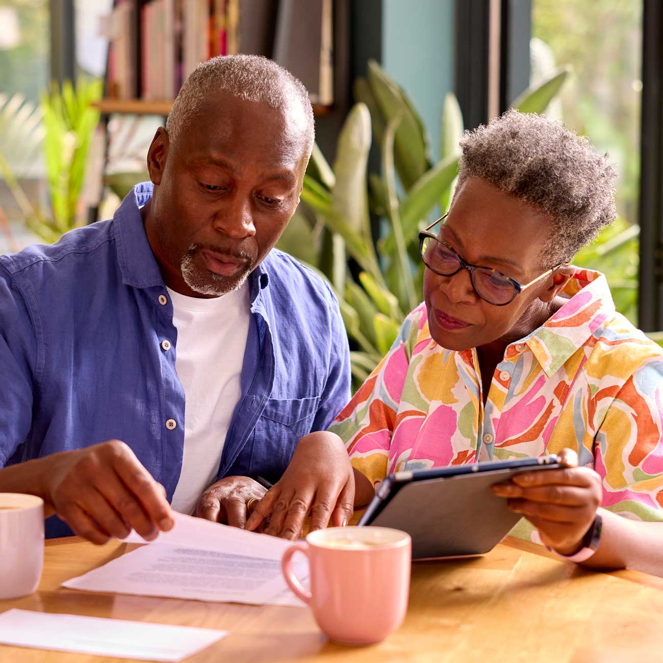 Older couple reviewing paperwork and using a tablet at home to explore disability support services