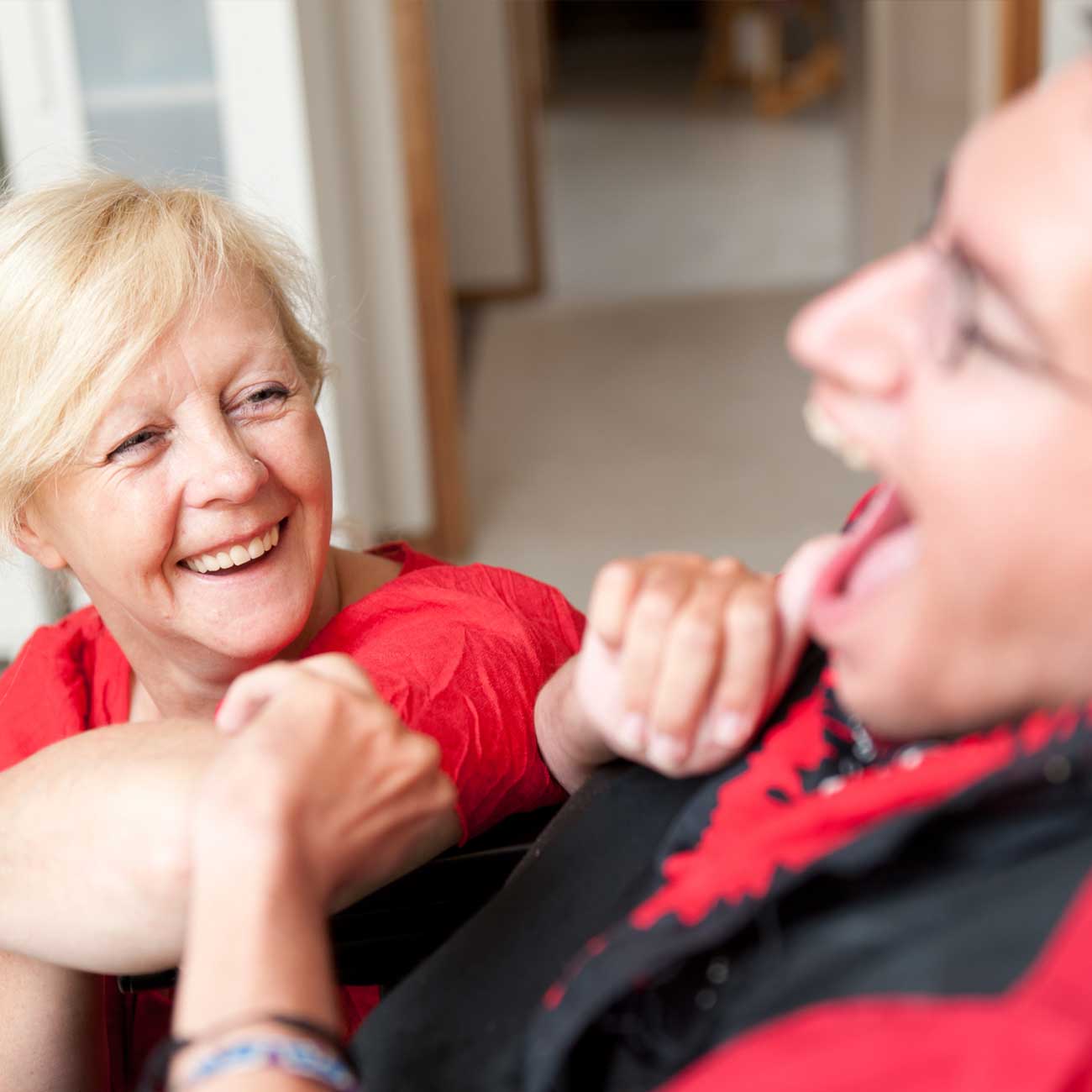 Smiling caregiver laughing with a young adult with disabilities in a home setting