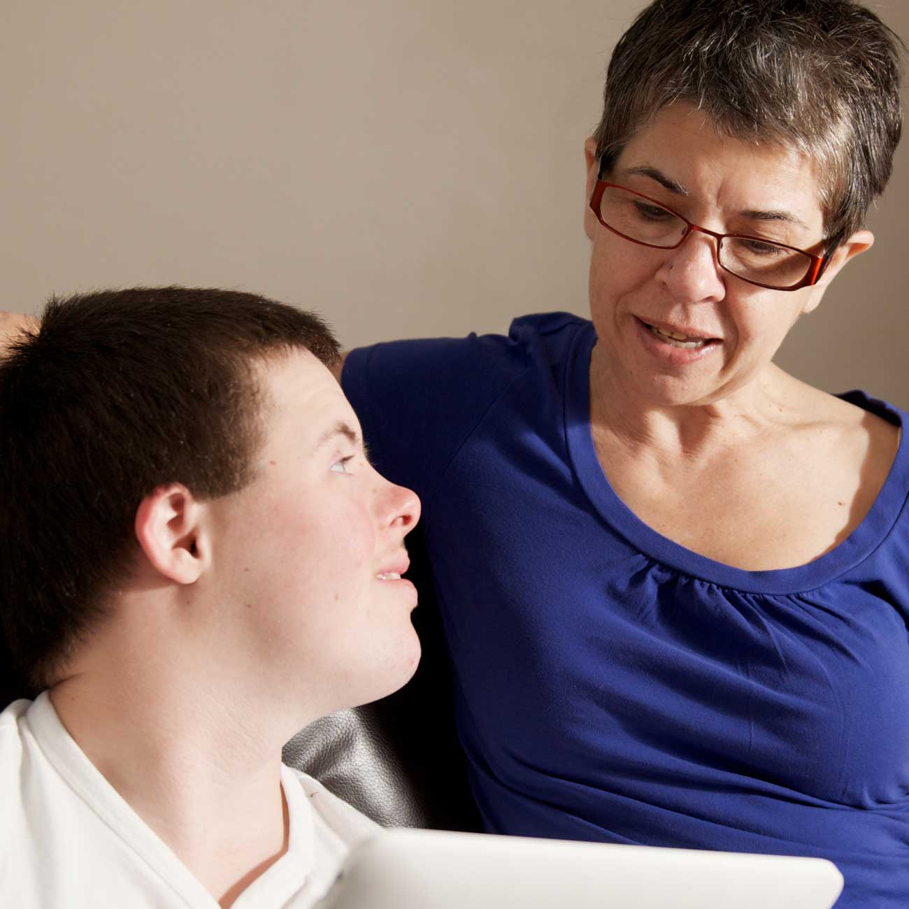 Supportive woman talking with a young man with Down syndrome while using a laptop together
